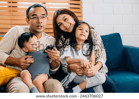 Family time is joy laughter and togetherness. A young family watches TV at home on a modern sofa with the father mother brother and sister all sharing precious moments of happiness.