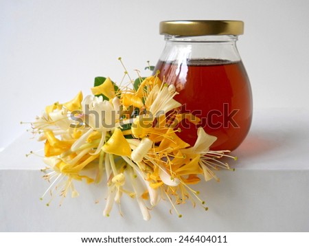 Honey in a glass bottle and honeysuckle flowers.