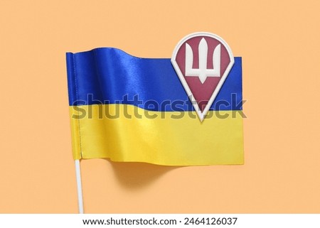 Military badge of Ukrainian army with trident and Ukraine flag on beige background