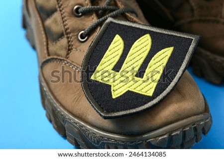 Military boots and badge of Ukrainian army with trident on blue background