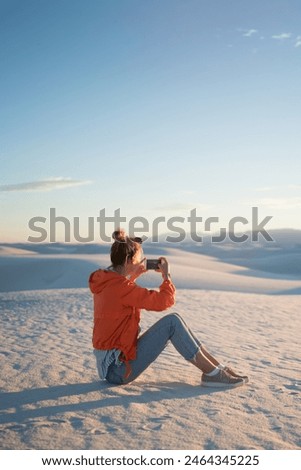 Young hipster girl using smartphone camera for taking picture of white dunes desert at susnet, woman photographing on telephone camera exploring nature view  during journey to famous landmark of USA