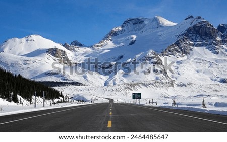 Scenic view of an empty asphalt road leading across scenic Banff National Park in the Canadian Rocky Mountains. Gorgeous wintry landscape and mountains surround the famous Icefields Parkway route.