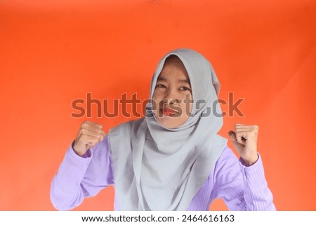 Portrait of an Asian Muslim woman with an enthusiastic and powerful boxing stance, isolated on an orange background