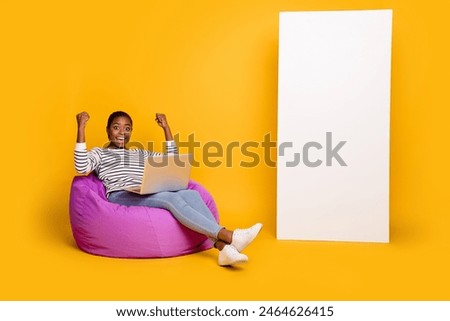 Full length photo of young lady use laptop rejoice luck ecstatic fists hands sit purple beanbag isolated over yellow color background