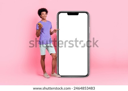 Full size photo of handsome guy wear t-shirt pants hold smartphone directing at touchscreen empty space isolated on pink color background