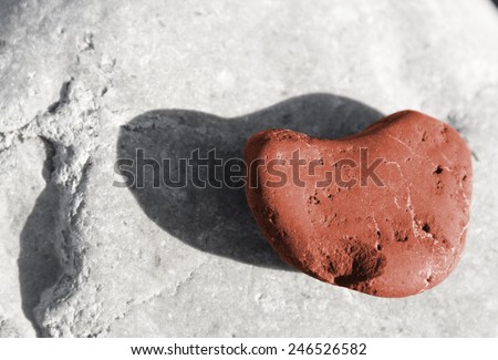 Red stone heart among river or sea pebble stones, background desaturated, Valentine's Day