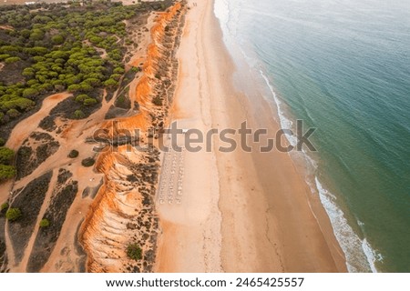 Algarve, Portugal coastline with sandy beach,  Atlantic Ocean waves and red cliffs at sunset. Aerial drone view.