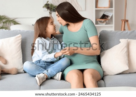 Little girl with her pregnant mother kissing on sofa at home