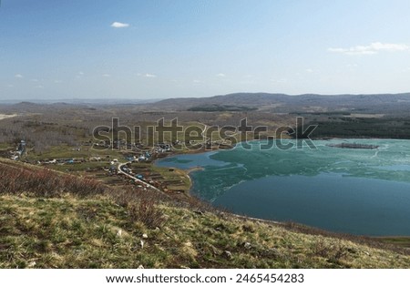 A small colorful Bashkir village (Russia) on the shore of a lake with melting ice. View from above