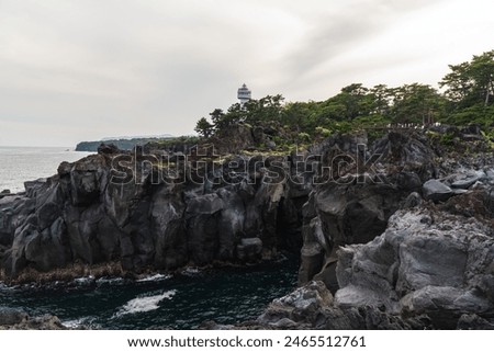 A beautiful coastal area in eastern part of Japan. A clear blue sky and an orange sunrise reflects on the sea water. A big rock formation in the coast line. Island from the distance.