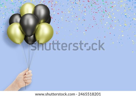 Female hand holding bunch of shiny golden and black balloons on blue background with confetti
