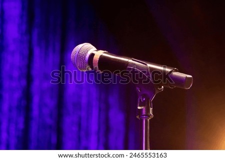 black Mic microphone mike with round head chrome on a stand ready for performer set against velvet blue curtain and a stagelight spotlight in bottom corner in theatre on stage