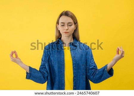 Mindful peaceful woman meditating, keep hands in mudra gesture, eyes closed, relax hold fingers in yoga sign, isolated on yellow wall