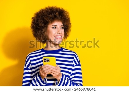Photo of nice young girl hold phone look empty space wear striped shirt isolated on yellow color background