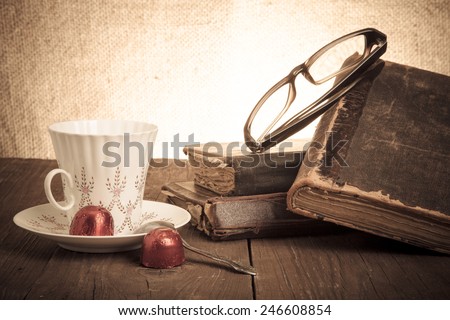 Cup of coffee, shokolad, glasses and stack of old books on the old wooden table. Toned.