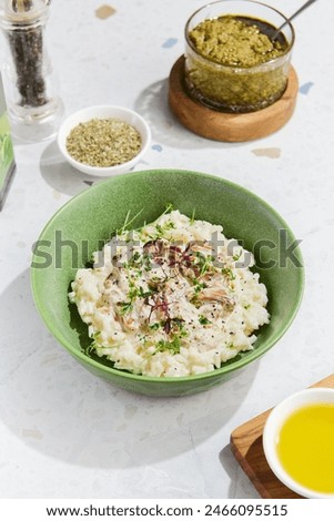 Mushroom Risotto with Fresh Herbs in a Green Bowl on Marble Table Enhanced with Condiments and Light Highlights.