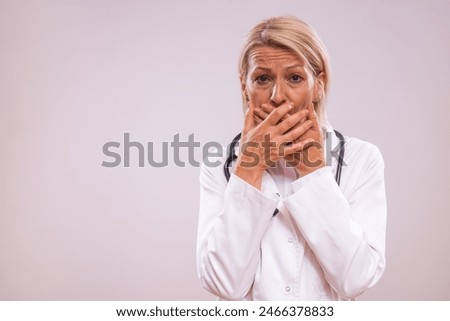 Portrait of  shocked mature female doctor covering mouth with hands.