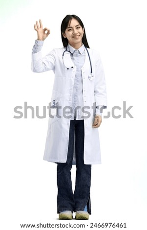 A female doctor, full-length, on a white background, shows an ok sign