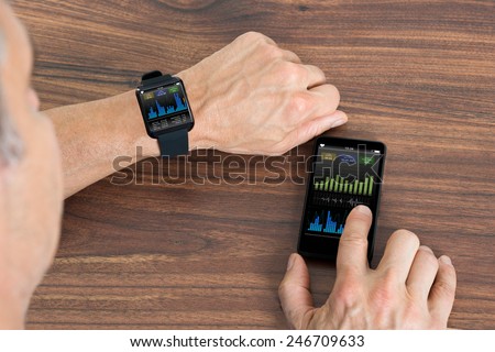 Close-up Of Mature Man With Smartwatch And Cellphone Showing Heartbeat Rate Sitting At The Table Royalty-Free Stock Photo #246709633