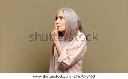 senior woman asking for silence and quiet, gesturing with finger in front of mouth, saying shh or keeping a secret