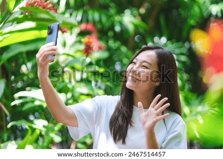 Portrait image of a young woman using mobile phone to take a selfie in the garden