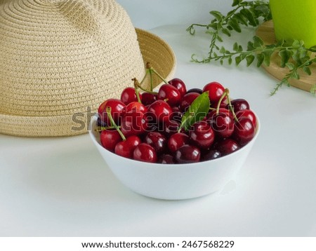 straw hat and a ripe cherry on a white table. 