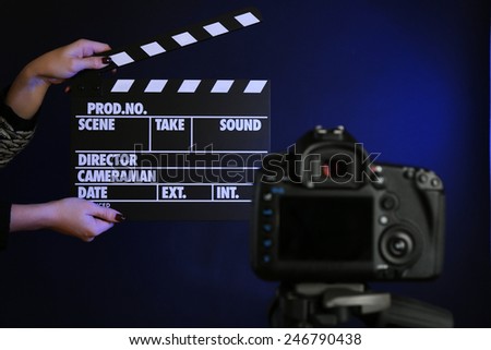 Hands with movie clapper board in front of camera on dark background