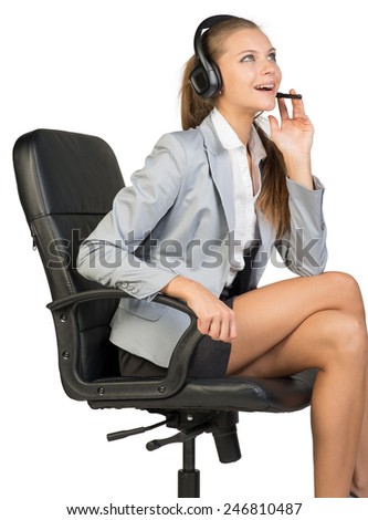 Businesswoman in headset sitting on office chair, with her fingers on microphone boom, looking upwards, laughing. Isolated over white background