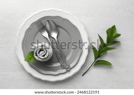 Stylish setting with cutlery, napkin, branch and plates on light textured table, top view. Space for text