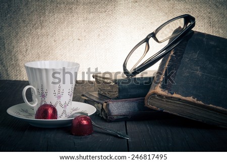Cup of coffee, shokolad, glasses and stack of old books on the old wooden table. Toned.