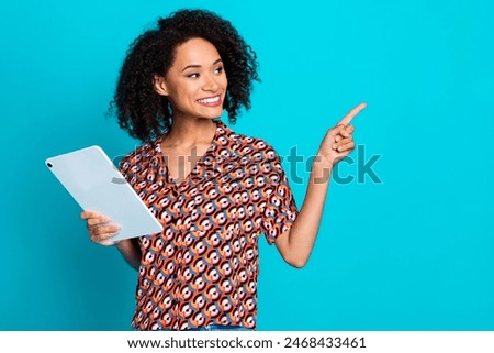 Photo of cute woman with perming coiffure dressed blouse holding tablet look directing at empty space isolated on blue color background