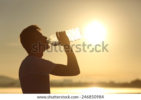Profile of a fitness man silhouette drinking water from a bottle at sunset with the sun in the background Royalty-Free Stock Photo #246850984