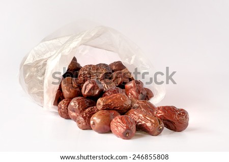 Red dates from transparent plastic bag on white background.