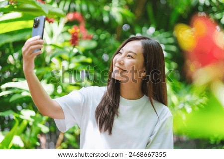 Portrait image of a young woman using mobile phone to take a selfie in the garden