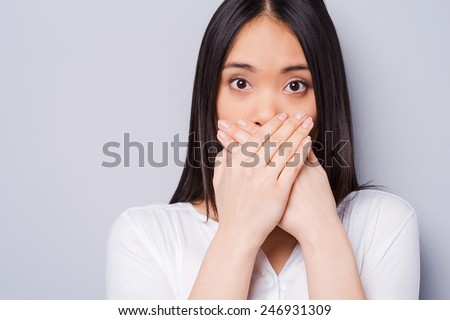 Oops! Surprised young Asian woman covering mouth with hands and staring at camera while standing against grey background Royalty-Free Stock Photo #246931309