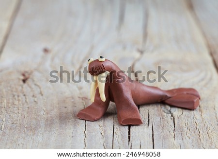 Plasticine world - little homemade brown walrus on a wooden background, selective focus and place for text 