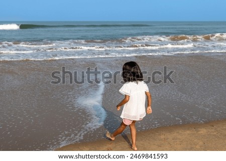 A carefree little girl stands on the sandy beach, her hair tousled by the ocean breeze. Sun-kissed and joyful, she gazes out at the horizon.