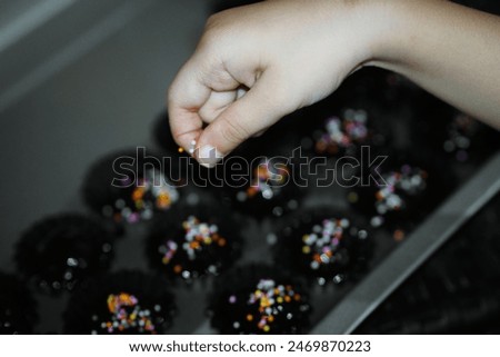 A child's hand is sprinkling topping onto a cake