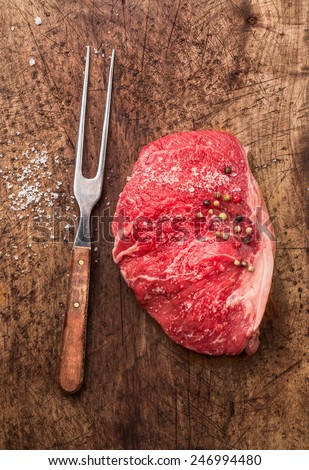 Raw meat Striploin steak with fork, salt and pepper on old wooden background, top view
