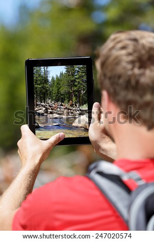 Hiking hiker man taking pictures of forest on digital tablet computer. Young adult doing mobile photography of nature landscape in Yosemite National Park, California, USA.