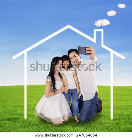 Portrait of happy family using a mobilphone to take self portrait under a dream house symbol