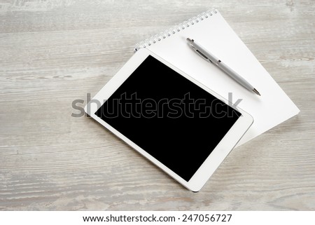 Tablet with notebook on wooden table and pen