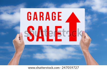 Two hands holding brown cardboard with garage sale on blue sky background