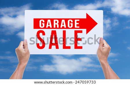Two hands holding brown cardboard with garage sale on blue sky background