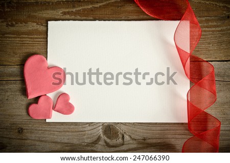 piece of paper lying with hearts and ribbon on a wooden background