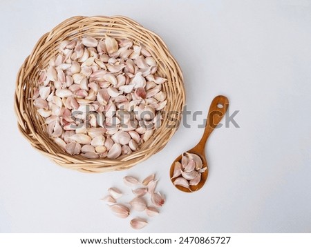 Garlic cloves are in a wicker basket and a wooden spoon is placed on a white background. It is a very beautiful picture.