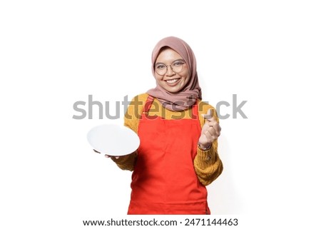Young Asian muslim woman in apron standing and holding empty white plate isolated on white background