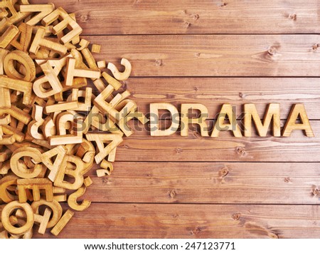 Word drama made with block wooden letters next to a pile of other letters over the wooden board surface composition