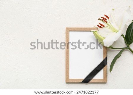 Blank funeral photo frame and white lily on light background