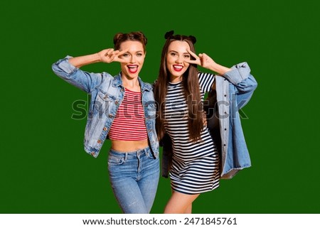 Two careless carefree cheerful charming glad positive grinning friendly optimist brunette hair lady look at camera stand isolated on yellow vivid background give v-sign near eyes make hollywood smile